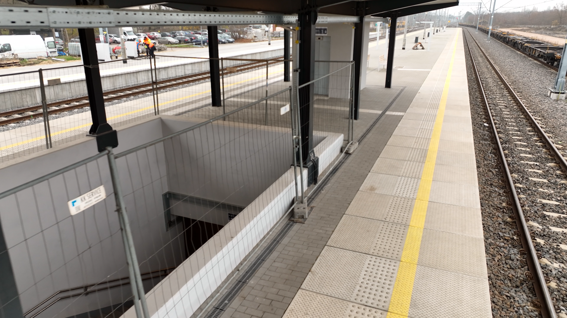 Ilustracja przedstawia przejście pod torami. Widoczny jest peron kolejowy oraz schody prowadzące w dół, ogrodzone barierkami.