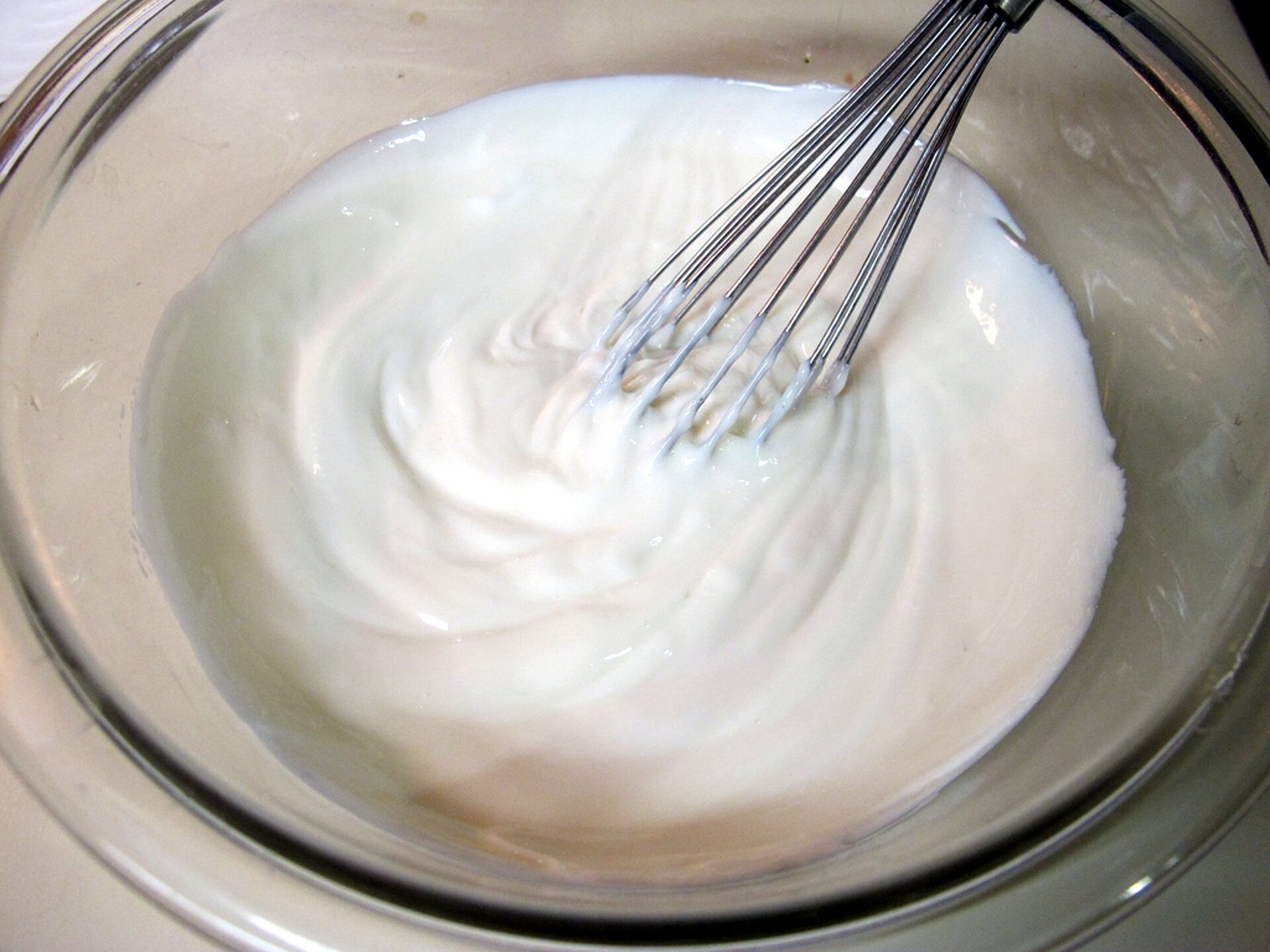 Na zdjęciu znajduje się miska z metalową trzepaczką oraz jogurtem.