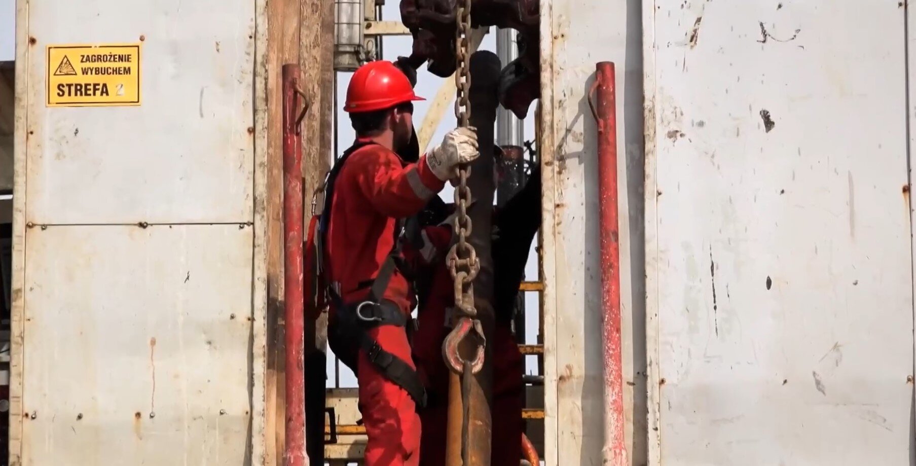 Ilustracja procesu wciągania. Mężczyzna ubrany w czerwony kombinezon wciąga metalowy element przy pomocy haka.