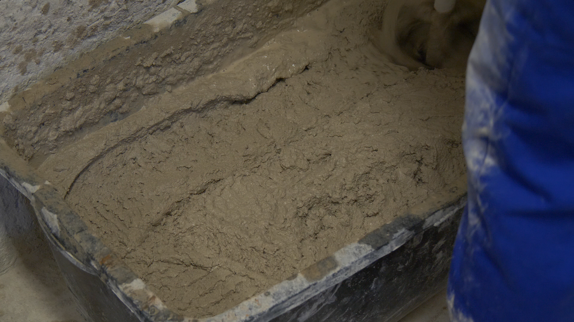 Zdjęcie przedstawia odlew elementu architektonicznego wykonany z betonu. W dużym plastikowym pojemniku znajduje się płynny beton.