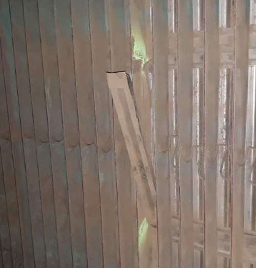 Na obrazku przedstawiono nieszczelność, która została wykryta za pomocą proszku fluorescencyjnego. Na ścianie widnieje element, który odstaje od innych, a wokół niego jest proszek fluorescencyjny.