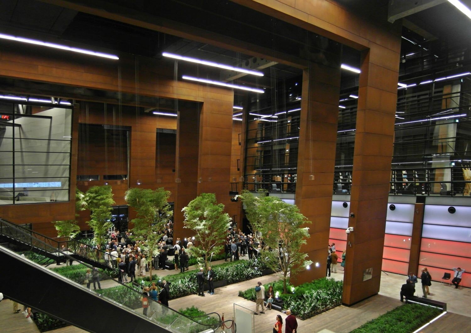 Fotografia przedstawiająca zwiedzających w holu ECS. W pomieszczeniu znajdują się posadzone drzewa i inne rośliny, ruchome schody oraz miejsca do odpoczynku .