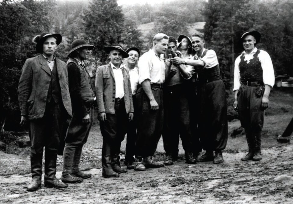 Zdjęcie przedstawia grupę dziewięciu młodych mężczyzn na tle porośniętych drzewami wzgórz. Kilku z nich uśmiecha się do obiektywu. Ubrani są nieformalnie stroje: mają koszule, kamizeli, niektórzy marynarki, spodnie, długie lub krótkie buty. Kilku z nich ma na głowach charakterystyczne góralskie filcowe kapelusze.
