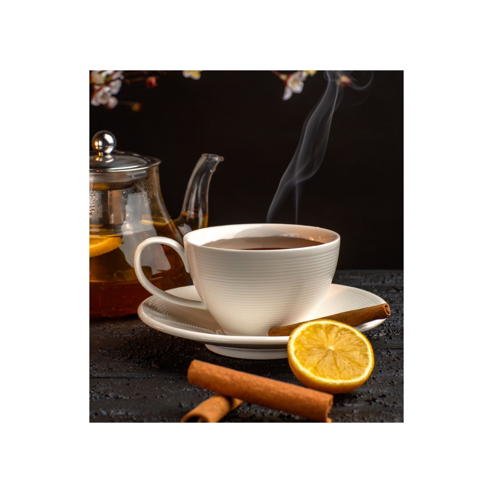 Zdjęcie przedstawia filiżankę z gorącą herbatą. Przed nią leżą plasterki cytryny i kora cynamonu.