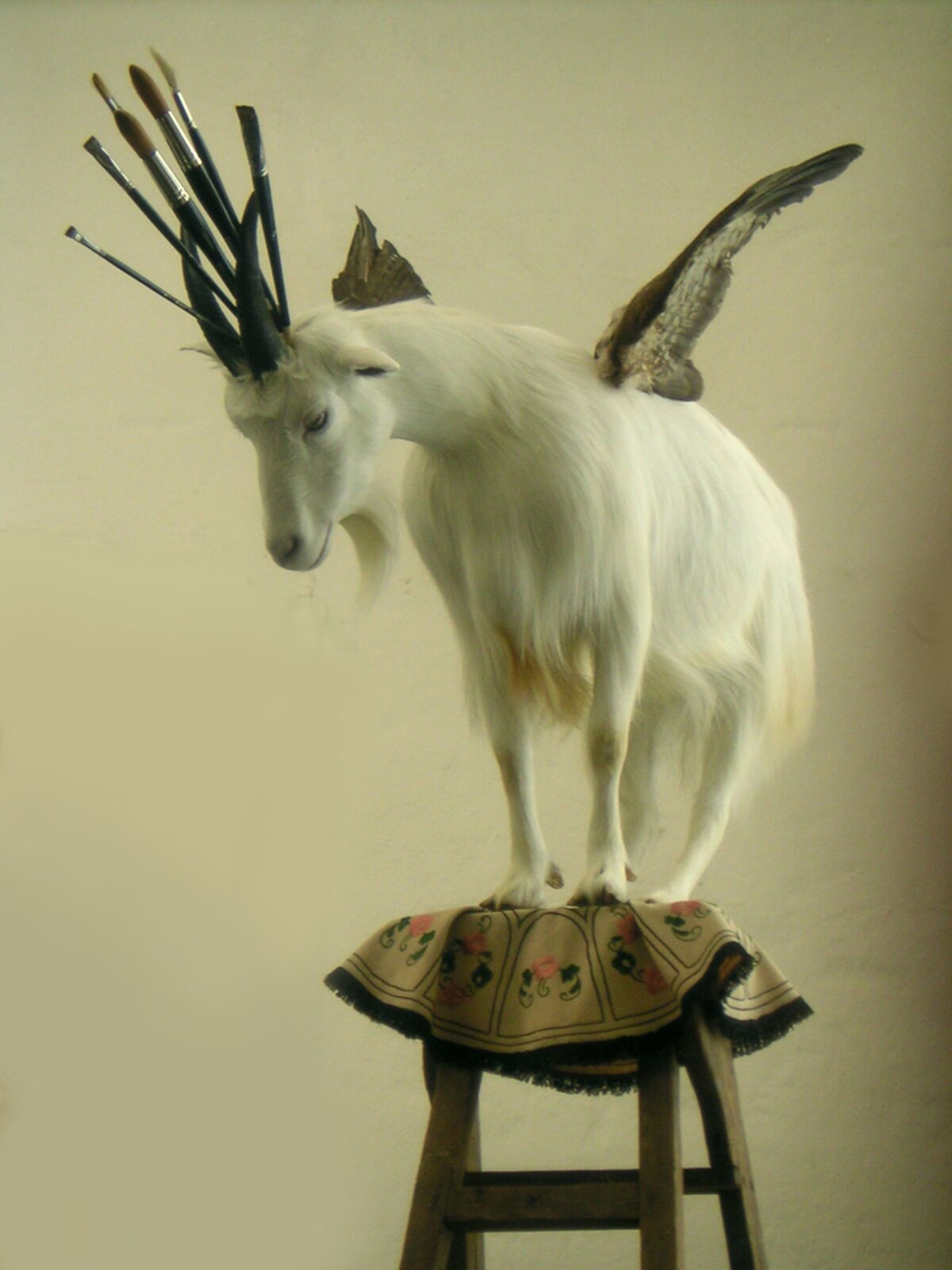 Ilustracja przedstawia dzieło Isma Kajandera „Kocham Paryż”. Asamblaż przedstawia kozę stojącą na szczycie rozkładanej, drewnianej drabiny, przykrytej haftowaną serwetą. Koza jest biała, a przy rogach ma umieszczone różnej wielkości artystyczne pędzle. Głowę ma pochyloną. Z jej grzbietu wystają dwa skrzydła.