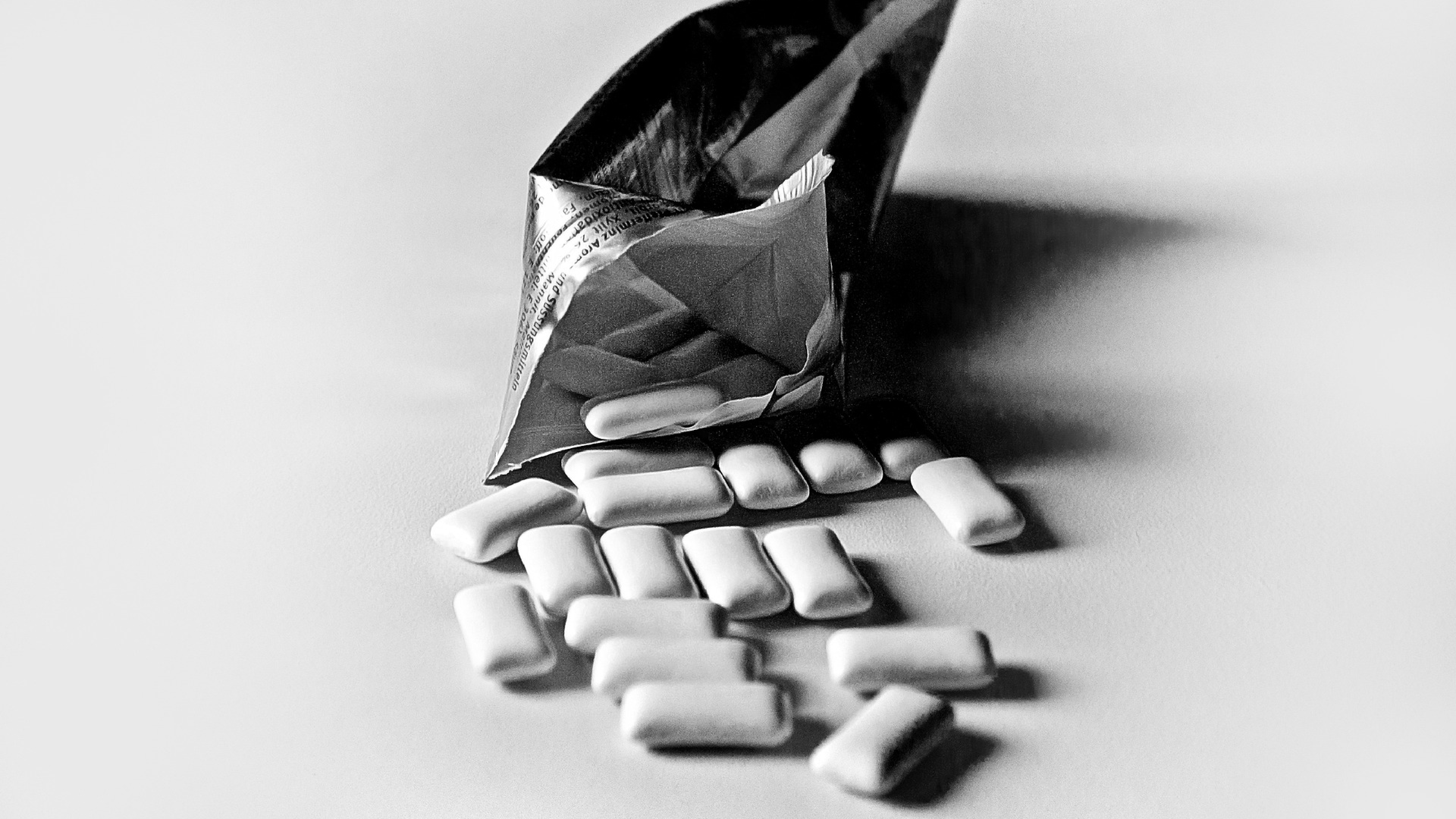 Zdjęcie przedstawia otworzone opakowanie gum do żucia. Część z nich została rozsypana na stole.