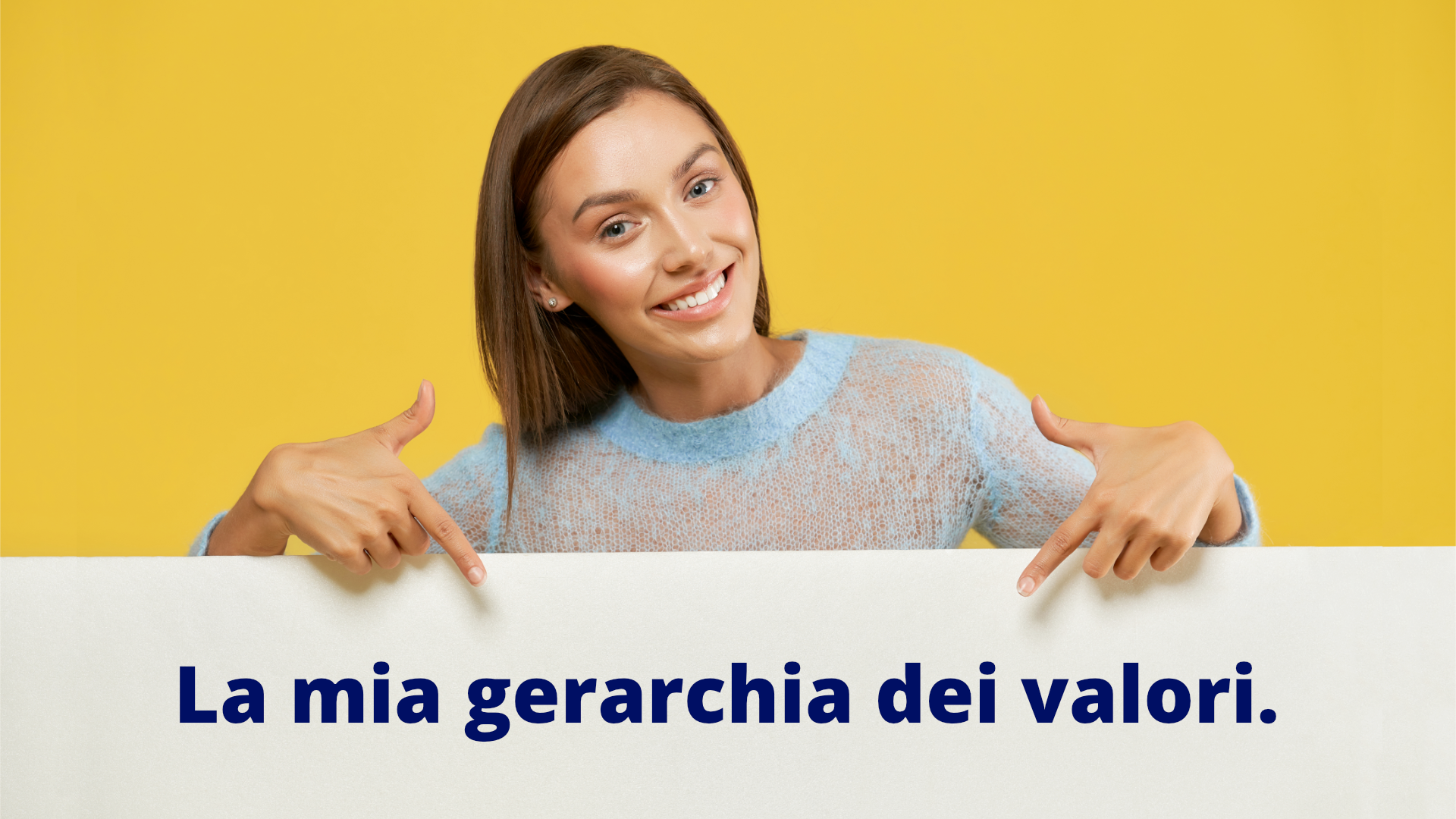 Na zdjęciu znajduje się młoda kobieta. Kobieta obiema rękami wskazuje na napis: "La mia gerarchia dei valori."