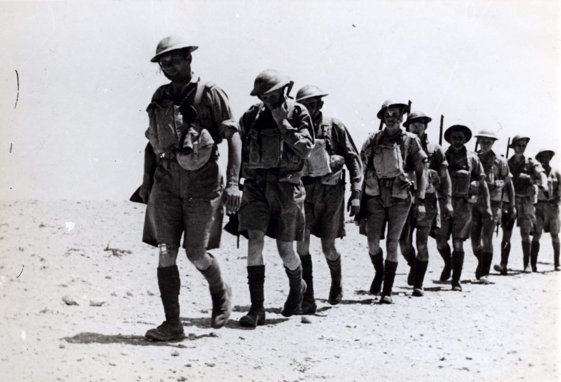 Zdjęcie przedstawia oddział żołnierzy idących jeden za drugim przez pustynię.