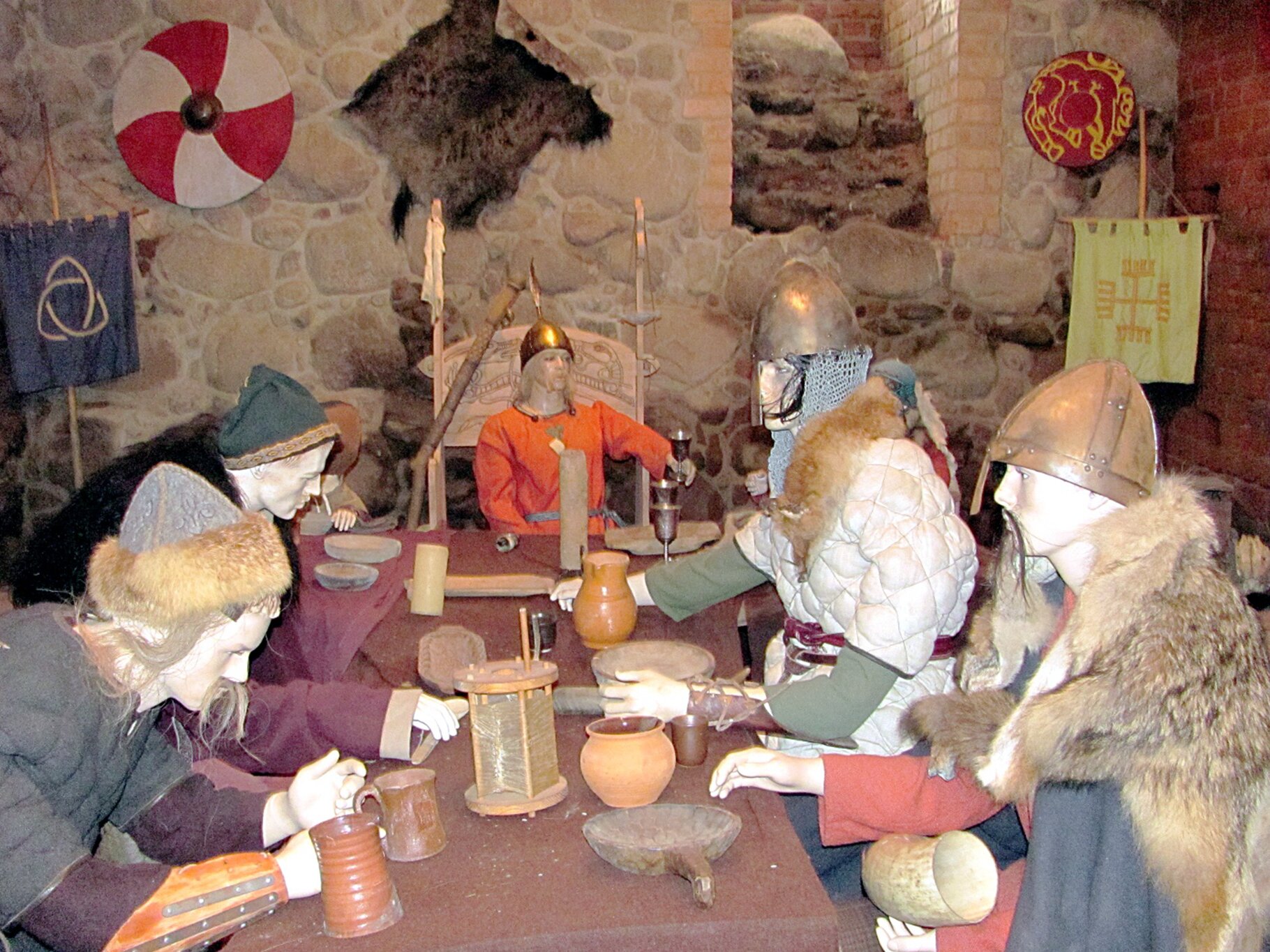 Fotografia przedstawia stałą wystawę z muzeum w Mysiej Wieży. Manekiny w strojach wojów siedzące przy stole.