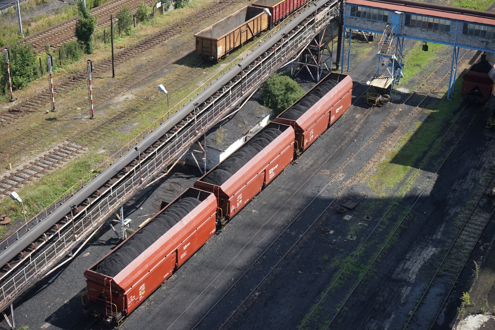 Na zdjęciu przedstawiono transport węgla przy pomocy kolei. Widoczne na zdjęciu wagony są załadowane węglem. Wagony stoją na szynach. Po lewej stronie zdjęcia znajduje się przenośnik taśmowy. Po prawej puste tory.Poniżej zdjęcia widoczny jest przycisk multimedialny z nagraniem audio. Treść nagrania jest zgodna z tytułem zdjęcia.
