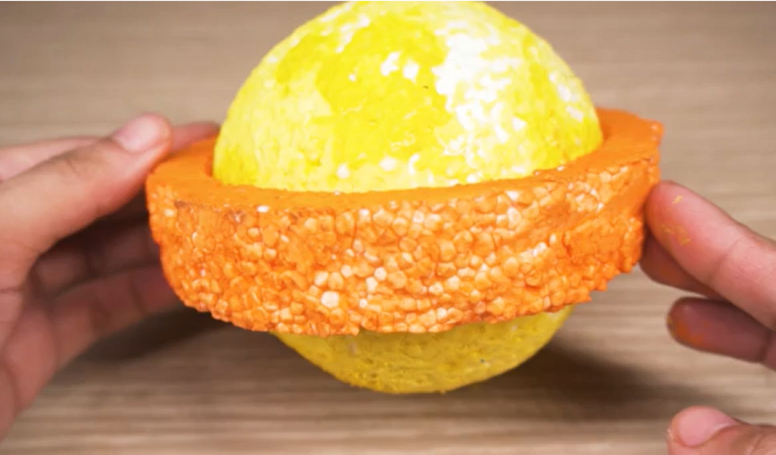 Zdjęcie przedstawia żółtą kulę z pomarańczowym pierścieniem wokół.