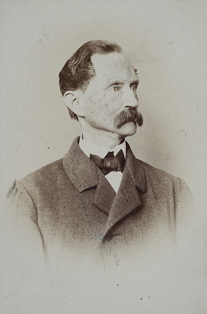 czarno‑biała fotografia przedstawia Hipolita Cegielskiego. Ma on krótkie ciemne włosy i dużego wąsa. Jest ubrany w garnitur i muszkę. 