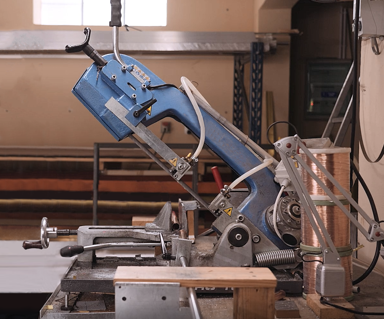 Zdjęcie przedstawia przecinarkę taśmową. Jest to urządzenie, które łączy się ze stolikiem jednym z końców. Za drugi koniec można przecinarkę unosić. W dolnej części przecinarki znajduje się ostrze, do którego doprowadzana jest woda. Przecinarkę opuszcza się ręcznie w celu przecięcia metalowego elementu.