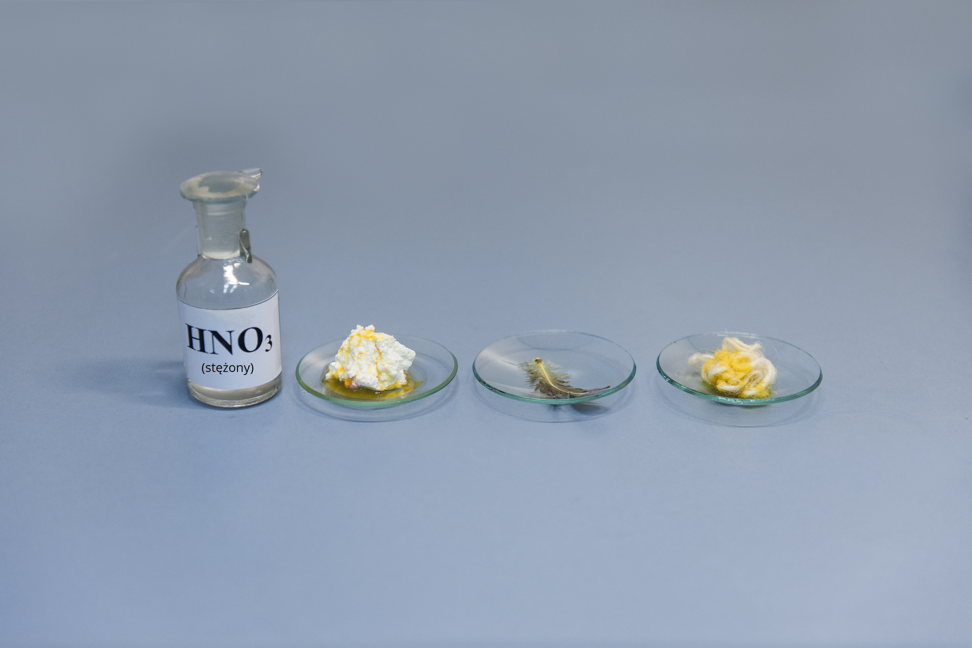 Drugie zdjęcie w galerii przedstawia stan końcowy tego samego eksperymentu, co na pierwszej ilustracji. Wszystkie trzy próbki charakteryzują się intensywnie żółtym zabarwieniem w miejscach, w których doszło do ich kontaktu z kwasem azotowym(pięć).