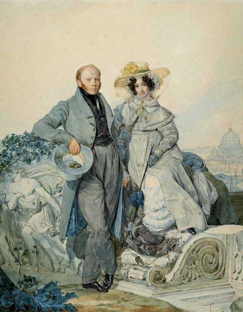 Obraz przedstawia mężczyznę i kobietę opierających się o dużą rzeźbę porośniętą bluszczem. Mężczyzna jest ubrany w jasno‑niebieski płaszcz i ciemną kamizelkę. Ma krótkie rude włosy i baki. W prawej ręce trzyma jasno‑niebieski kapelusz. Kobieta jest ubrana w jasno‑niebieską grubą suknię. Ma niebieskie rękawiczki i szeroki kapelusz. Ma czarne kręcone włosy.