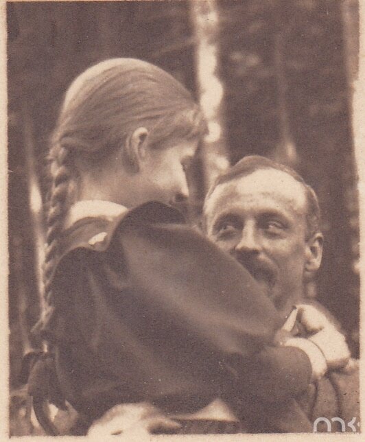 Fotografia przedstawia mężczyznę w sile wieku trzymającego w ramionach dziewczynkę. Postać ukazuje lewy połprofil owalnej twarzy. Włosy mężczyzny są ciemne, proste, zaczesane na prawą stronę. Ma on lekko zmarszczone czoło, jasne brwi i oczy zwężone w uśmiechu. Patrzy na córkę. Nos mężczyzny jest prosty. Pisarz ma wąsy. Mężczyzna jest ubrany w marynarkę. Dziewczynka ukazuje prawy profil. Ma lekko opuszczone powieki i niewielki nos. Jej włosy są długie, zaplecione w warkocz. Dziecko obejmuje oburącz szyję mężczyzny. Dziewczynka jest ubrana w sukienkę. W tle ukazane są wysokie drzewa.