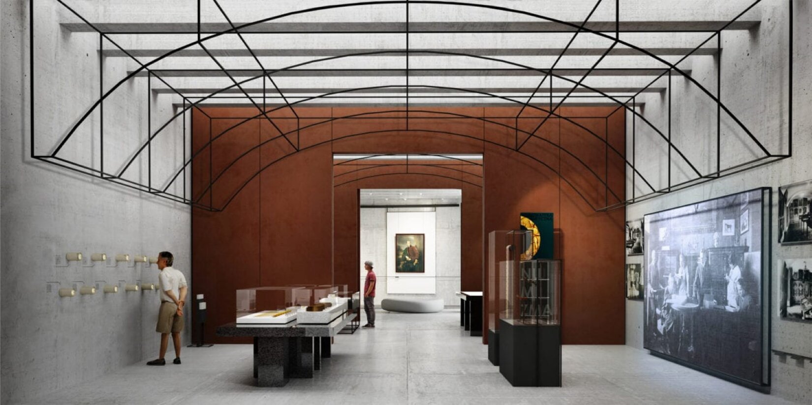 Fotografia ukazuje pomieszczenie muzeum, na jego środku znajdują się szklane gabloty z ekspozycjami. Po lewej stronie stoi mężczyzna, który spogląda przez wystające ze ściany tuby. Mężczyzna ubrany jest w krótkie spodenki w kolorze beżowym oraz białą koszulę. Po prawej stronie znajdują się czarno‑białe obrazy, jeden duży oraz cztery mniejsze. Nad pomieszczeniem, pod sufitem znajduje się czarna, metalowa konstrukcja. W oddali, na drugim planie znajduje się mężczyzna, który ubrany jest w szare spodnie, czerwoną koszulkę oraz czapkę z daszkiem. W kolejnym pomieszczeniu, na środku ściany wisi obraz, przedstawiający portret mężczyzny. 