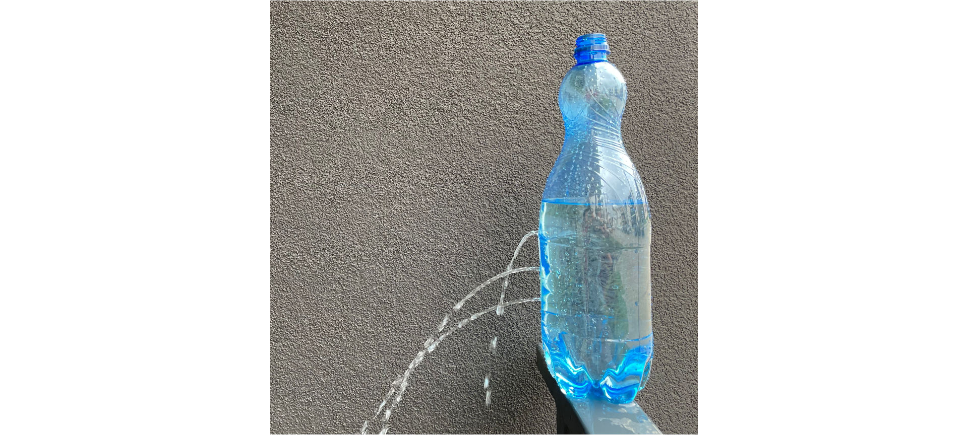 Zdjęcie przedstawiające butelkę wypełnioną wodą. Butelka przedziurawiona w trzech miejscach. Dziurki zrobione są w równych odległościach od siebie w pionie, na jednej linii. Strumienie wypływającej z tych dziurek wody posiadają różne ciśnienie w zależności od wysokości słupa wody w butelce, a więc strumień wypływający z dziurki najwyższej spada blisko butelki, a z najniższej - najdalej.