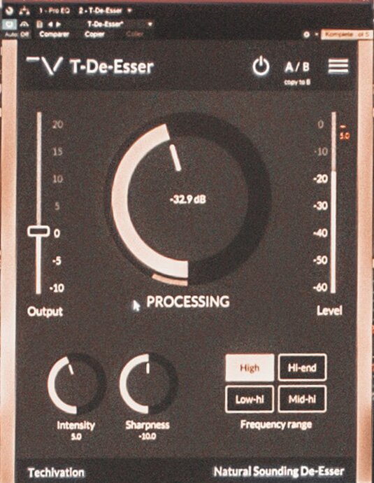 Na zdjęciu widoczny jest typ kompresora de‑esser. Widać prostokąt w pionie, z beżowymi bocznymi krawędziami, w środku matowo czarny. W prostokąt wpisane są od góry: po lewej stronie napis z białych liter T‑De‑Essser, na prawo symbol zasilania oraz duże litery A/B i cztery krótkie poziome kreski. Poniżej, w środku widoczna jest czarny okrąg obrazujący tarczę, którego lewa strona jest częściowo biała, w środku widoczny jest napis z białych cyfr i liter -32.9 db, zaś poniżej napis z dużych białych liter PROCESSING. Po lewej i prawej stronie widoczne są pionowe skale, na lewej z podpisem z białych liter Output, widoczne są cyfry od dołu -10, -5, 0, 5, 10, 15, 20, na prawej z podpisem z białych liter Level, widoczne są cyfry od dołu -60, -50, -40, -30, -20, -10, 0. Poniżej po prawej stronie widoczne dwa czarne okręgi obrazujące tarcze, których lewa strona jest częściowo biała, poniżej których widoczne są napisy z białych liter Intensity 5.0 pod prawą oraz Sharpness -10.0 pod lewą. Na prawo widoczne są cztery prostokąty w orientacji poziomej, dwa obok siebie i dwa poniżej nich. Lewy górny prostokąt jest biały z widocznym pośrodku napisem z ciemnych liter High. Pozostałe prostokąty są czarne z białymi krawędziami, z widocznymi pośrodku napisami z białych liter: prawy górny – Hi‑end, lewy dolny – Low‑hi, prawy dolny – Mid‑hi. Poniżej czterech prostokątów widoczny jest napis z białych liter Frequency range. Na samym dole widoczne są napisy z biały liter, po lewej Techivation, po prawej Natural Sounding De‑Esser.