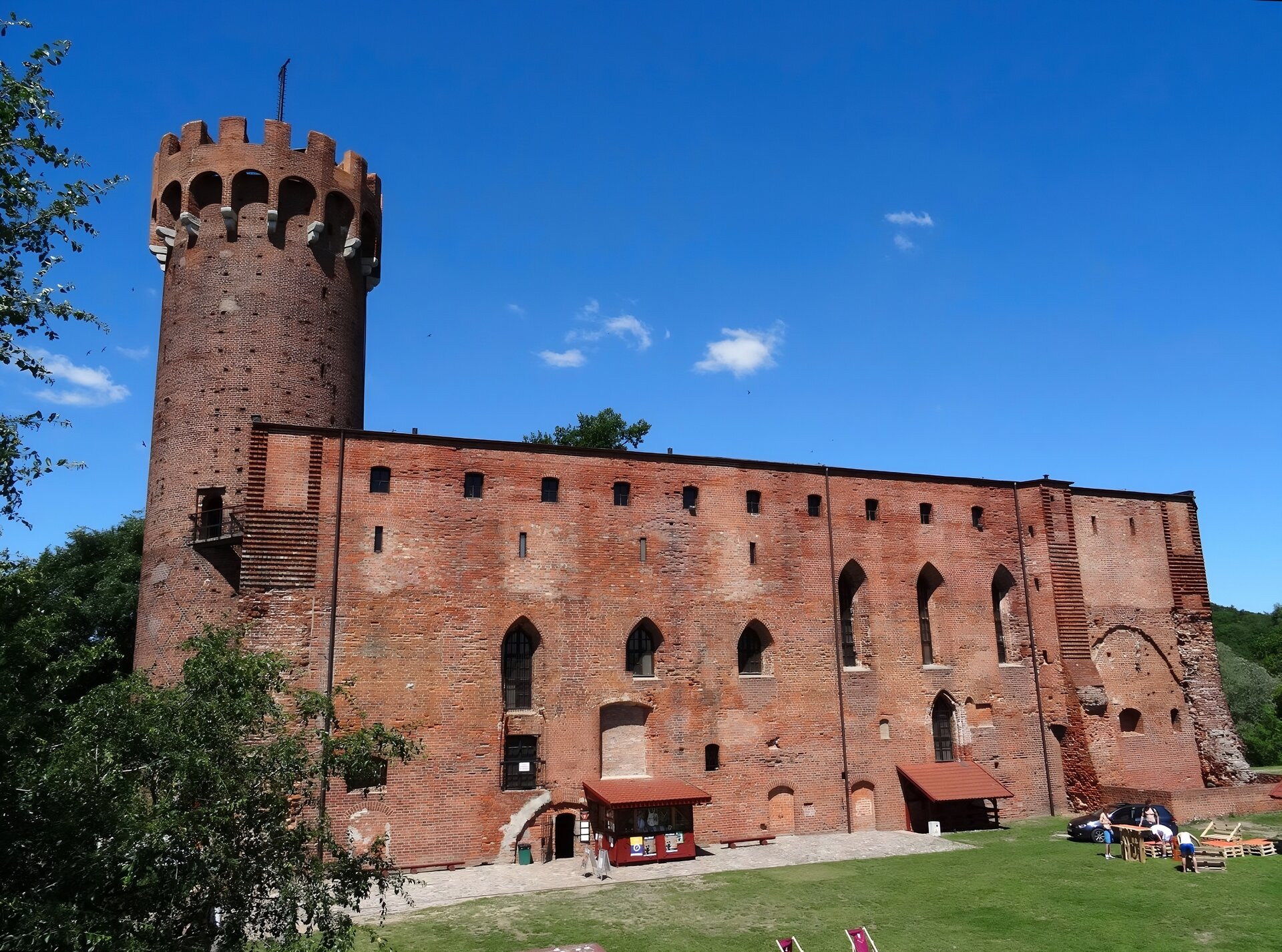 Zdjęcie przedstawia widok budynku głównego zamku wraz z wieżą. Na pierwszym planie widać mur, na drugim bryłę budynku głównegoa za nim wieża. Budynek został wzniesiony w stylu gotyckim, o czym świadczą widoczne ostre łuki oraz okna. Budynek wraz z wieżą został wzniesiony z cegły. 