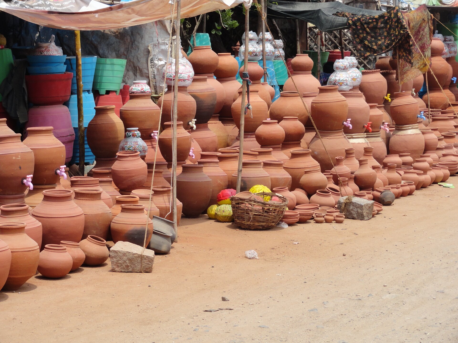Fotografia barwna przedstawiająca targ, na stoisku znajdują się naczynia gliniane oraz terakota.