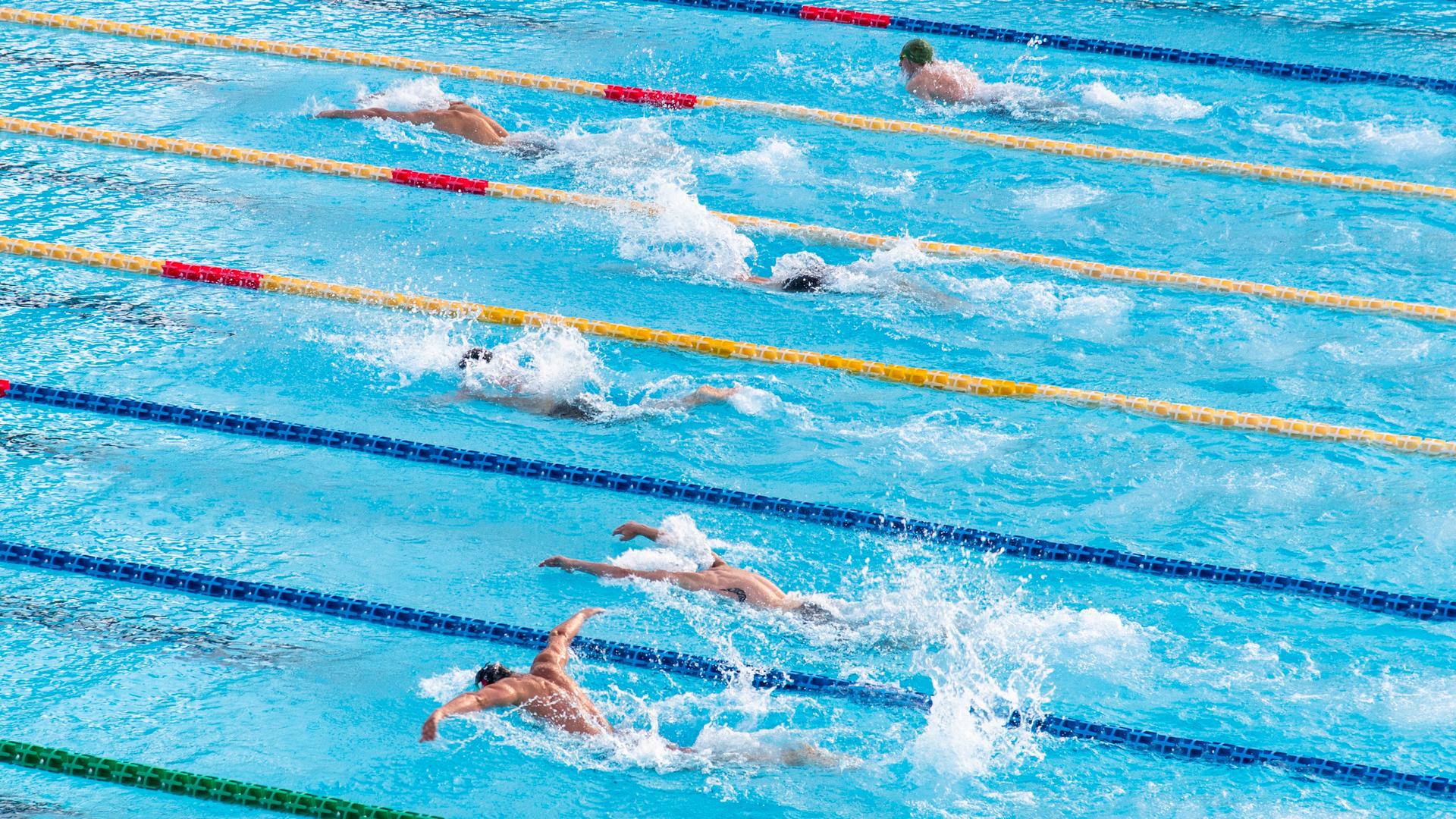 Zdjęcie przedstawia basen i sportowców rywalizujących w zawodach pływackich.