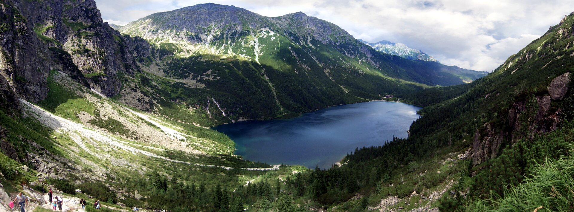 Na zdjęciu wysokie góry, szczyty skaliste, w dolinie jezioro o regularnym kształcie.