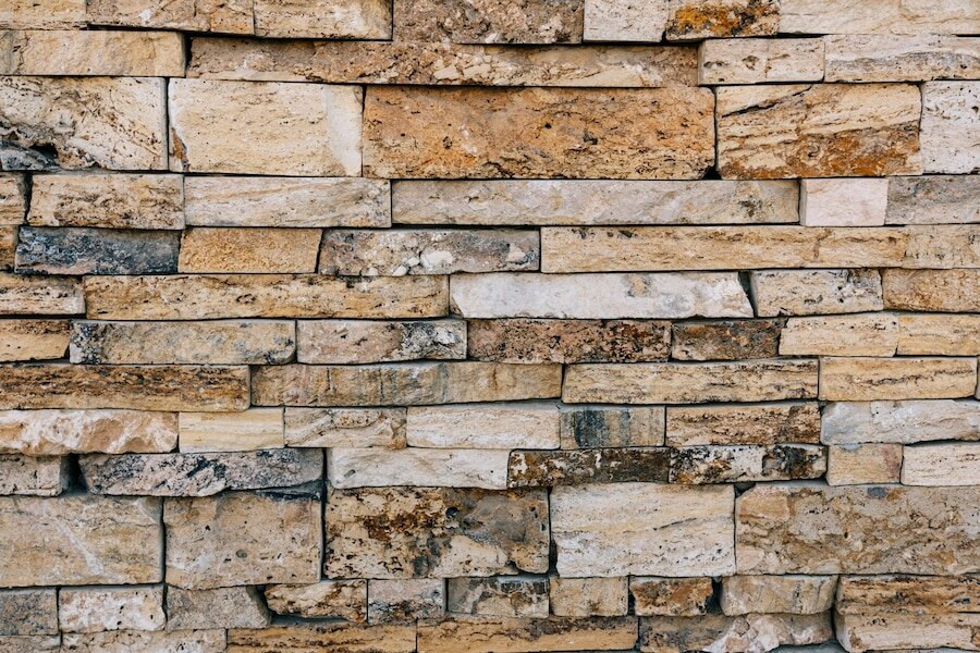 Zdjęcie przedstawia ścianę złożoną z kamieni o różnej wielkości i szerokości i fakturze grotowanej.