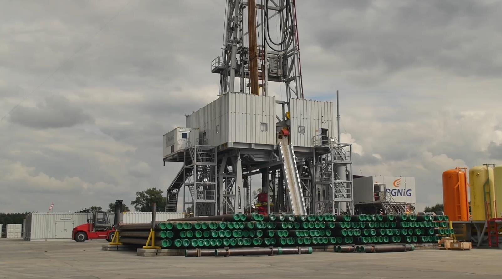 Na zdjęciu widoczny jest fragment wieżomasztu przedstawiający jego podbudowę. Wieżomaszt jest konstrukcją kratową przypominającą kształtem literę A. Widoczna na zdjęciu podbudowa na dolnej galerii wykonana jest z blachy falistej. Wieżoamszt osadzony jest na stalowym stelażu przypominającym cztery duże podpory. Po obu stronach wieżomasztu widoczne są schody prowadzące na galerię. Z przodu wieżomasztu zamontowana jest pochylnia.Przed wieżomasztem na placu wiertniczym magazynowane są czarne długie rury. Rury leżą na sobie.