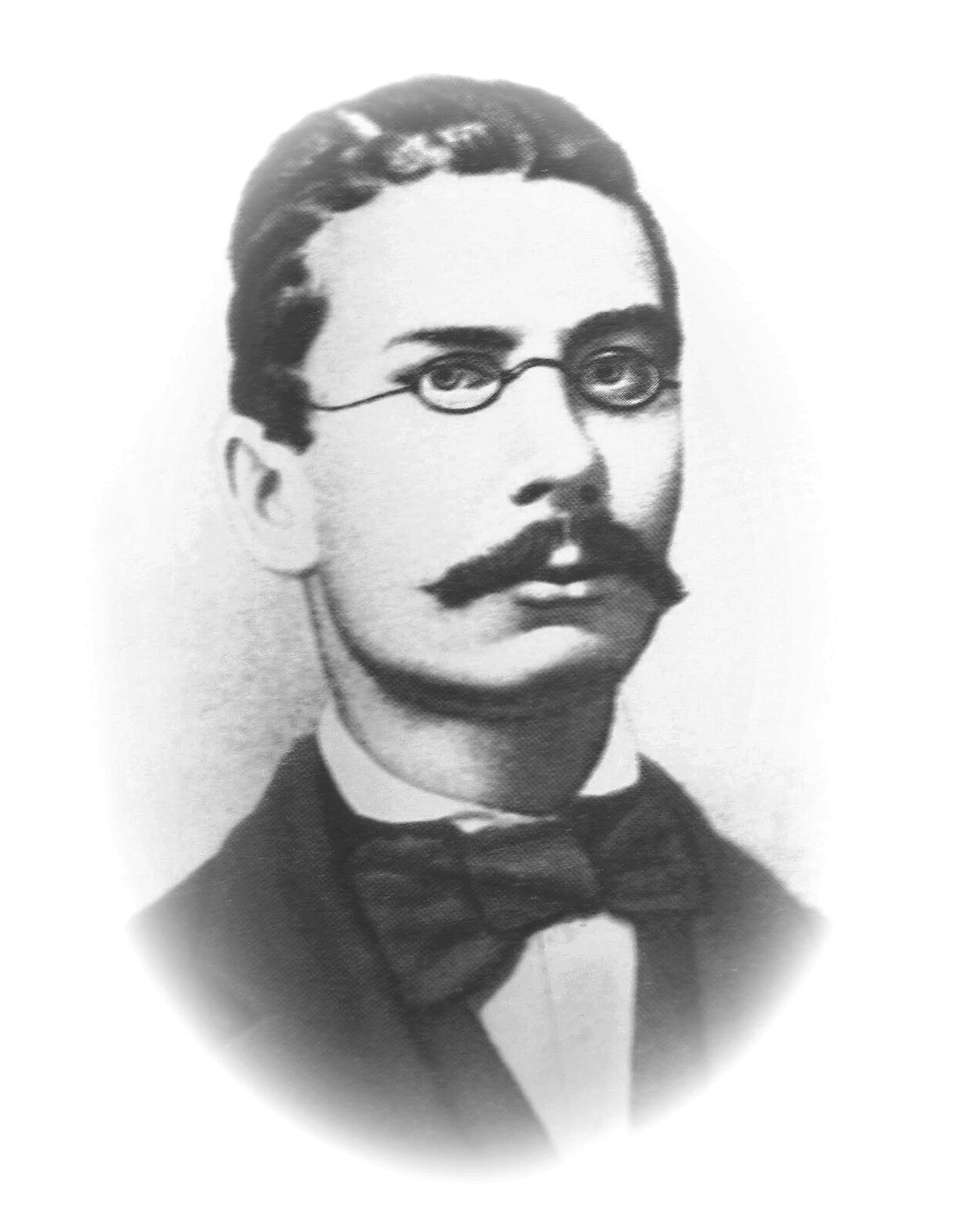 Na zdjęciu portretowym znajduje się młody mężczyzna. Ma on wąsy, okulary, krzaczaste brwi oraz gęste włosy. Jest ubrany w koszulę i marynarkę, na szyi ma muszkę.