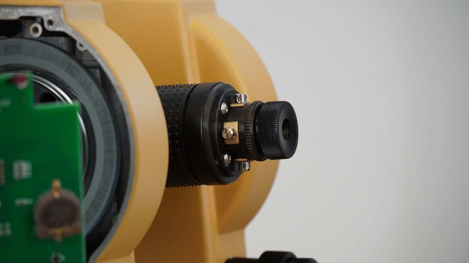 Zdjęcie przedstawia zbliżenie okularu po zdjęciu pierścienia. Widoczne są śruby umieszczone dookoła zespołu okularu z krzyżem nitek.