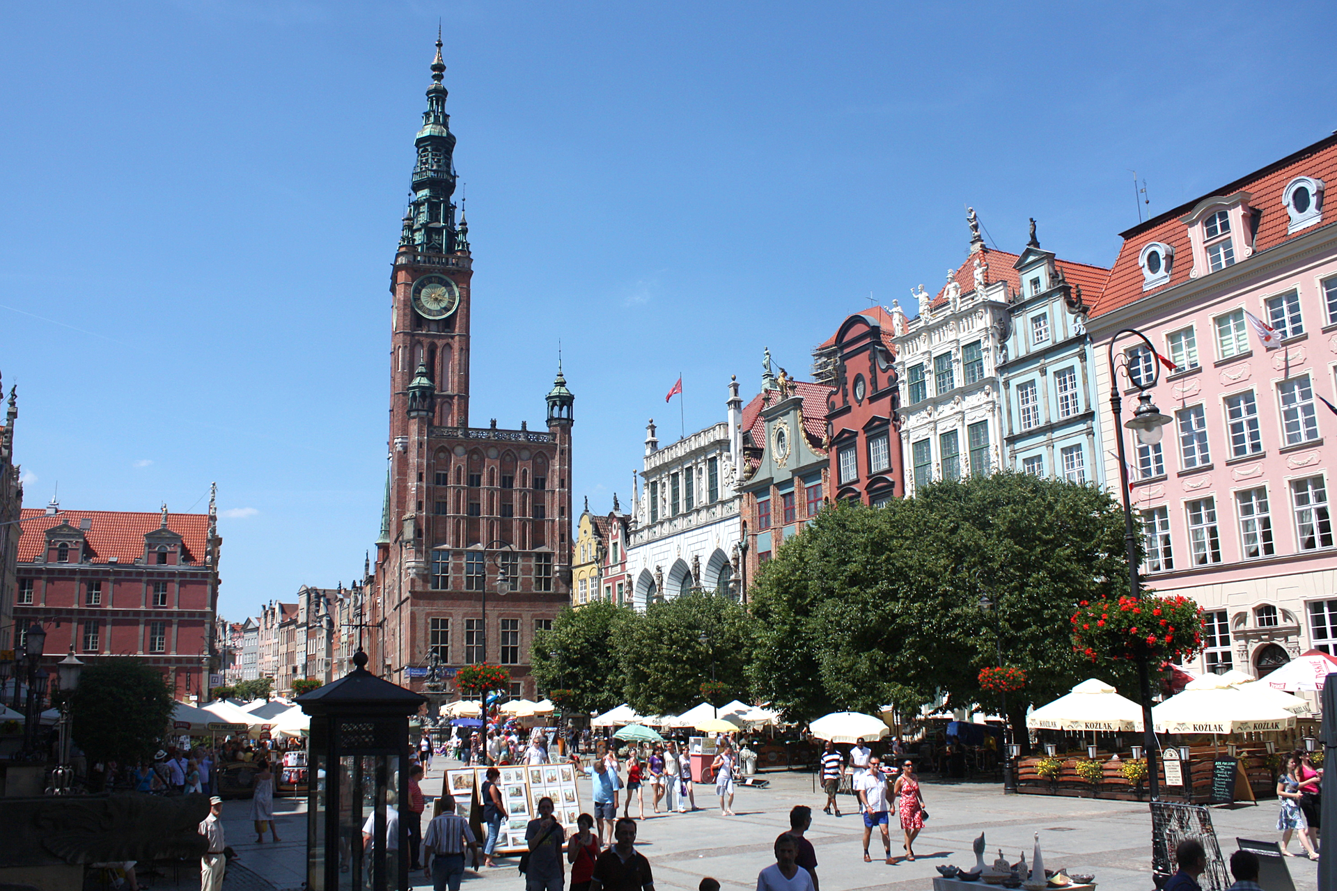 Zdjęcie ulicy Długiej oraz Starego miasta w Gdańsku. Widoczne wysokie kamienice wzdłuż ulicy oraz Ratusz w centrum Starego miasta. Sporo przechadzających się osób. 