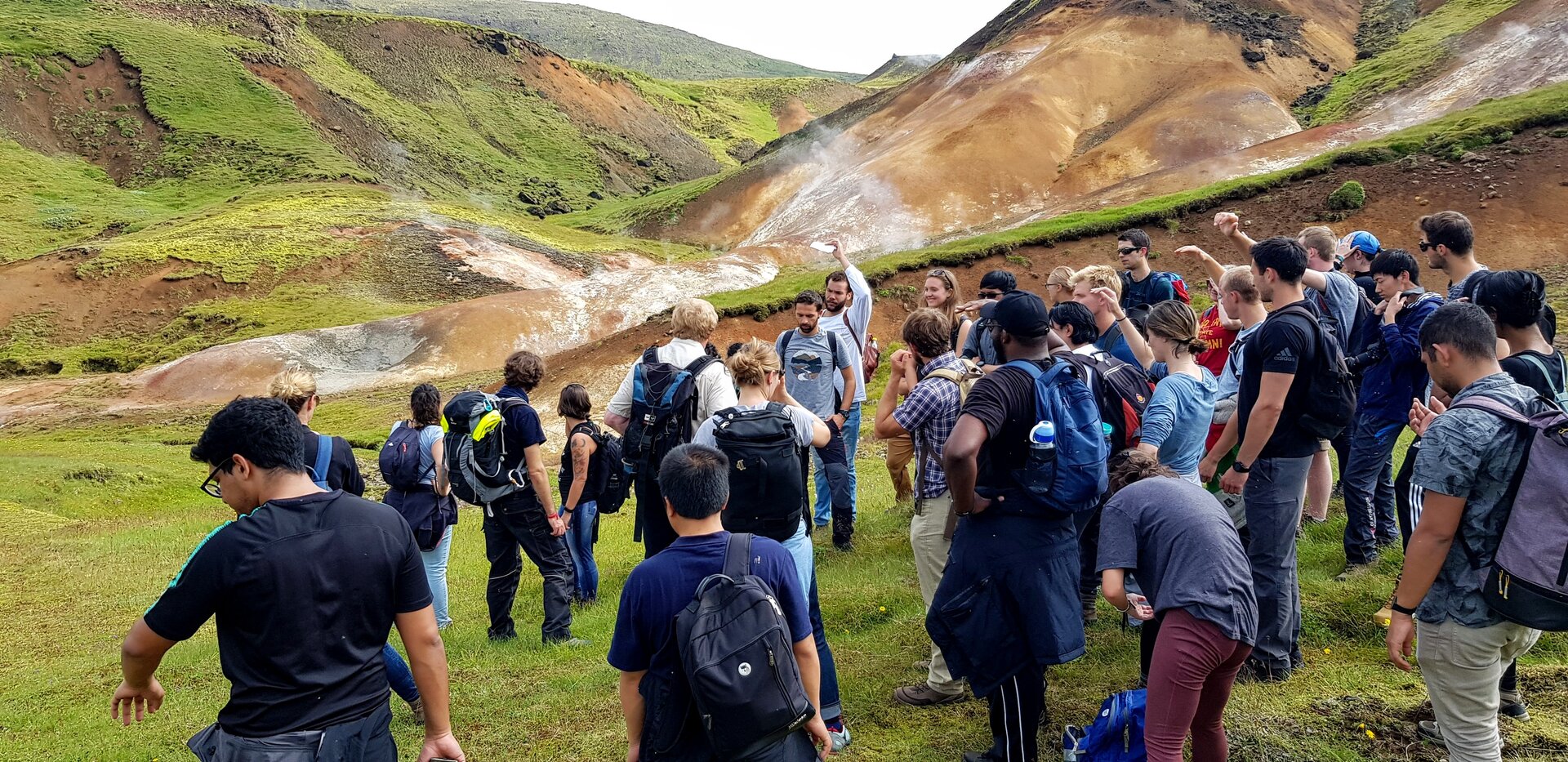 Zdjęcie przedstawia grupę uczniów na wycieczce w górach. Uczniowie stoją wśród gór, większość ma plecaki na plecach.