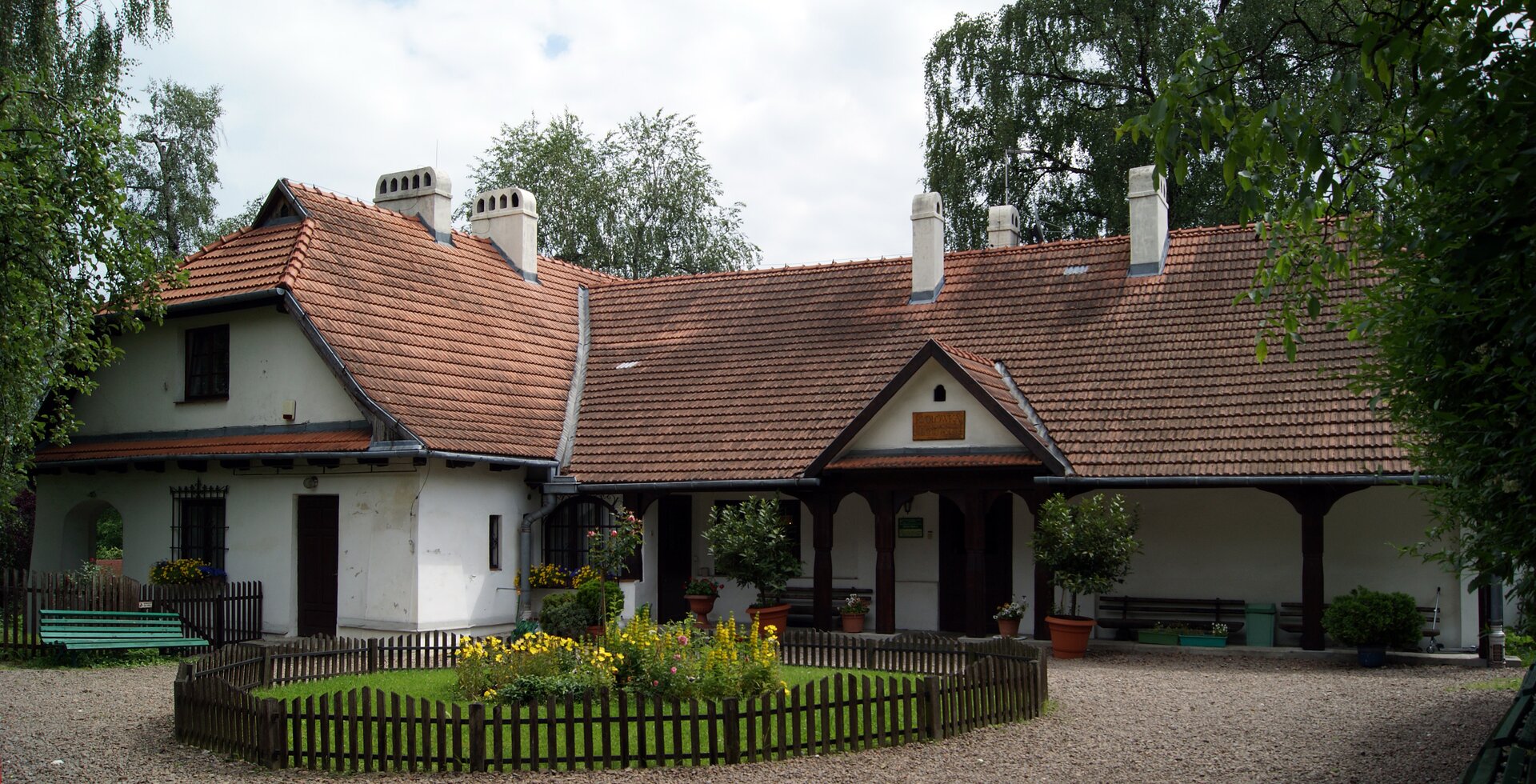 Na ilustracji znajduje się zabytkowy dwór Rydlówka. Parterowy budynek jest zbudowany na planie prostokąta. Przylegające skrzydło posiada piętro. Dach jest pokryty dachówką. Budynek ma alkierz wsparty na czterech drewnianych ozdobionych słupach. Przed dworkiem znajduje się kolista rabata z kwiatami, otoczona drewnianym płotkiem. 