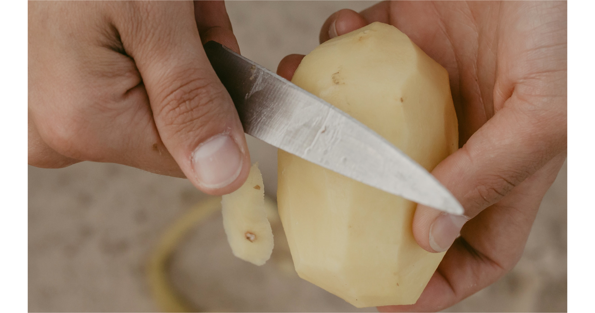 Zdjęcie przedstawia dłonie osoby obierającej ziemniaki. W jednym ręku znajduje się nóż, a w drugim ziemniak.