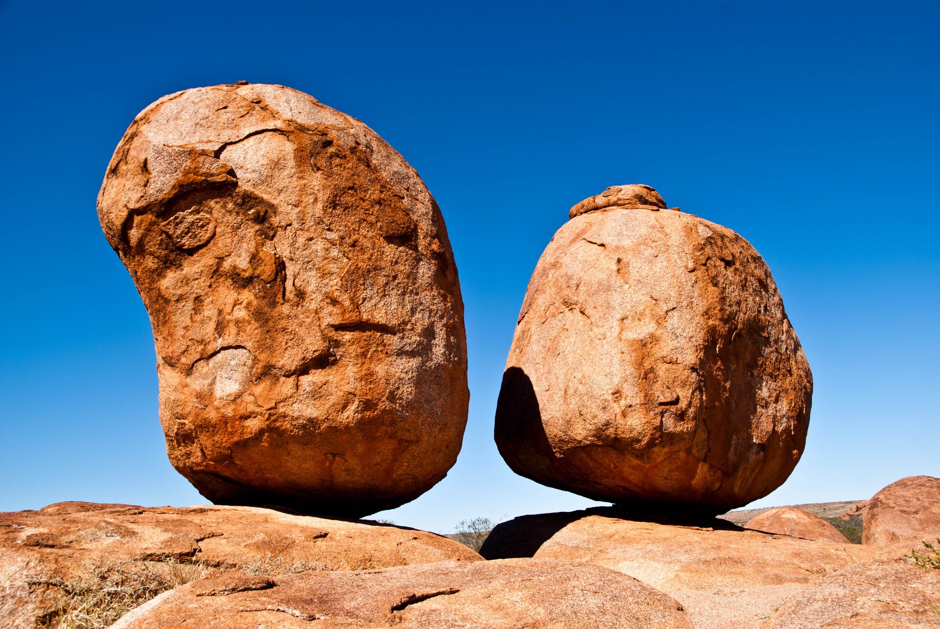 Na zdjęciu dwie owalne skały stojące na powierzchni skalnej. Skała z lewej strony nieco większa. Bloki skalne mają kolor ceglasty. W tle niebieskie niebo.