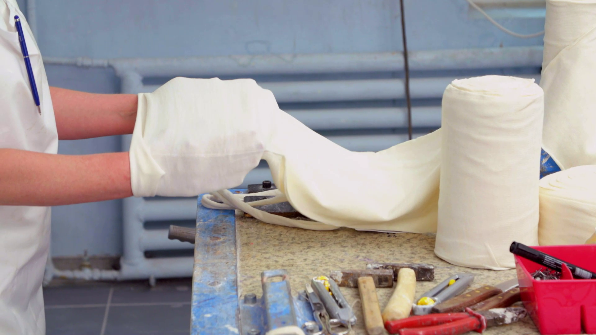 Zdjęcie przedstawia węża ortopedycznego, (węża protetycznego). Jest to materiał w postaci rękawa zwinięty w rulon. Jest nieco rozwinięty. Osoba na zdjęciu trzyma dłonie wewnątrz węża i rozciąga go na boki.