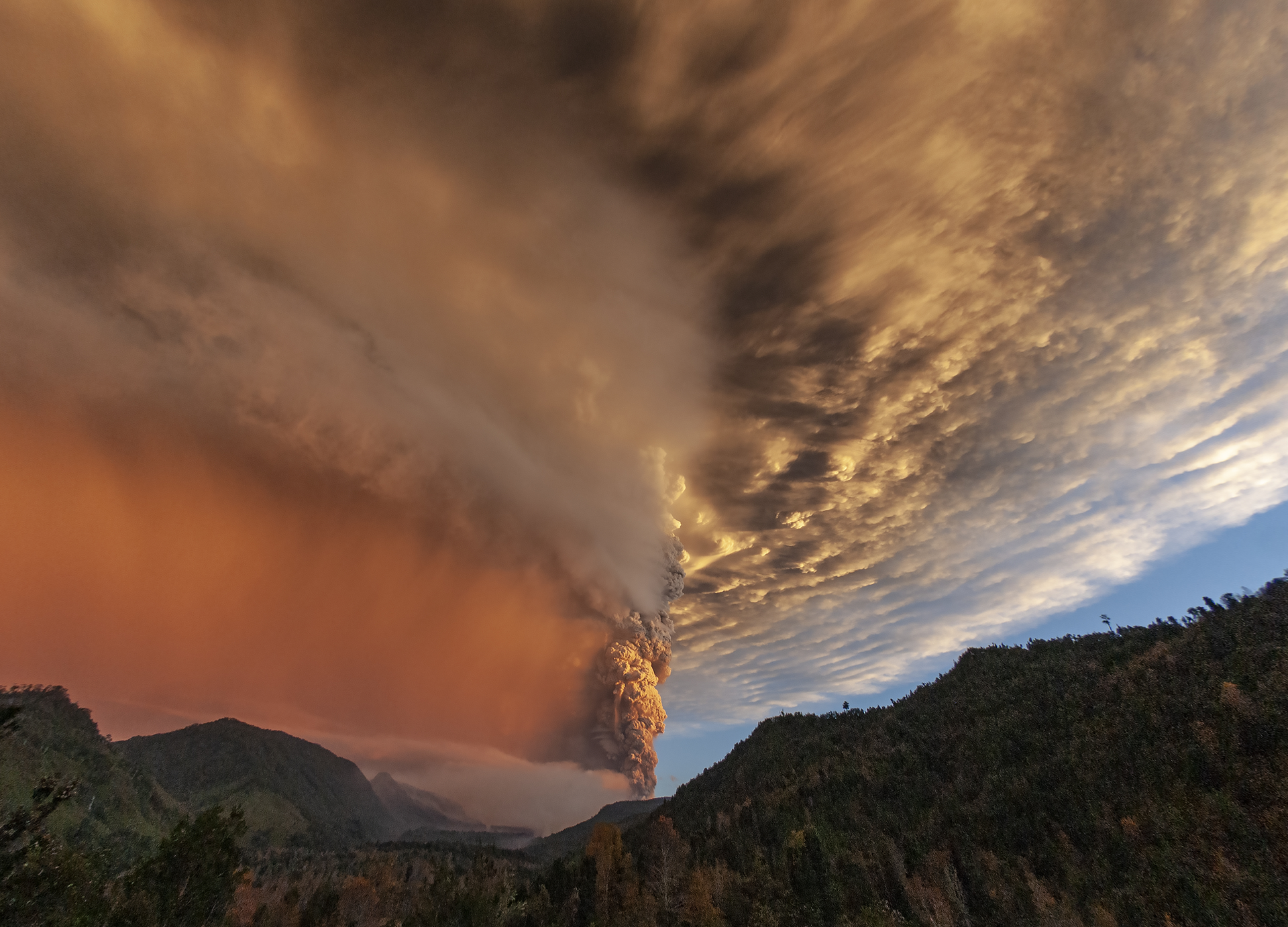 Zdjęcie przedstawia teren górzysty, nad którym unoszą się chmury, które kumulują się w centrum zdjęcia.
