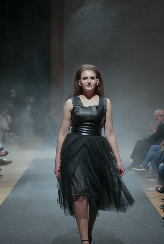 Zdjęcie przedstawia modelkę prezentującą ciemnoszarą sukienkę składającą się ze skórzanego topu i lejącej się, tiulowej spódnicy do kolan.