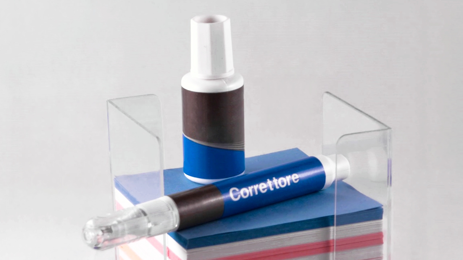 Zdjęcie przedstawia dwa rodzaje korektorów. Jeden to korektor w pędzelku, drugi to korektor w formie pisaka. Korektory leżą na plastikowym pudełku z kolorowymi karteczkami.