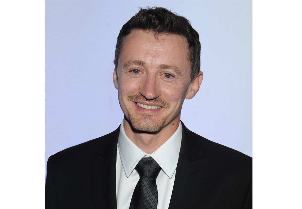 Fotografia barwna przedstawiająca uśmiechniętego Adama Małysza. Ma na sobie garnitur, patrzy wprost w obiektyw.