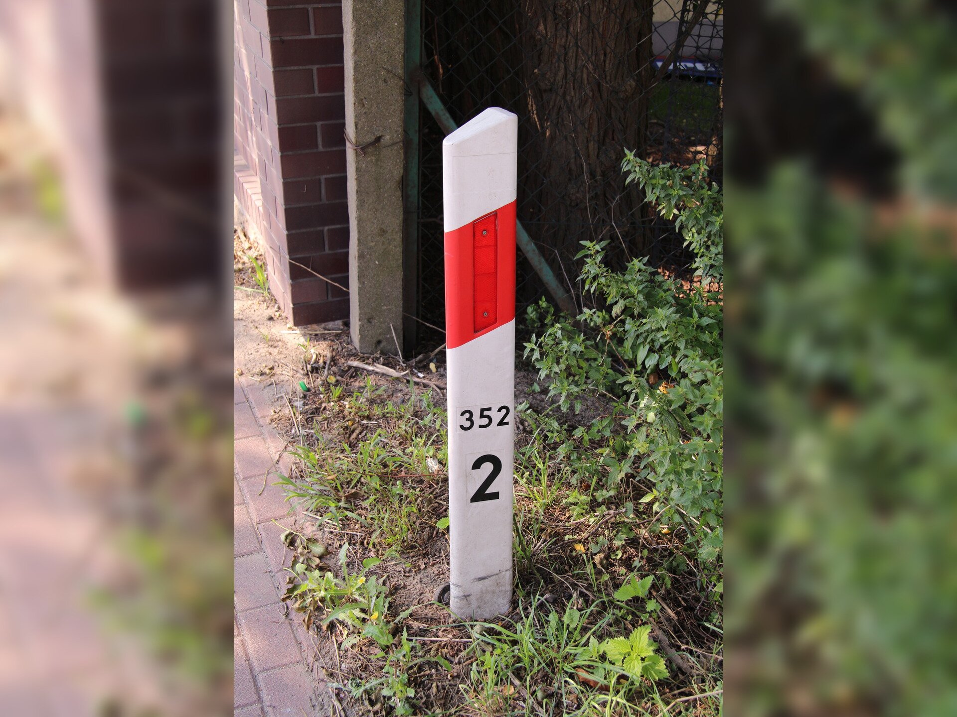 Fotografia przedstawia biało-czerwony słupek przydrożny, na którym umieszczono liczby oznaczające odległości.