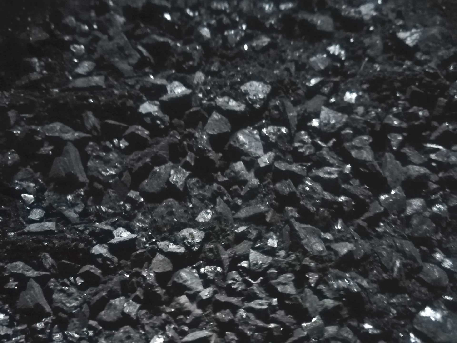 Zdjęcie przedstawia materiał przypominający wyglądem węgiel kamienny. Nieregularne odłamki materiału mają czarny kolor, gdzieniegdzie mają błyszczącą strukturę.