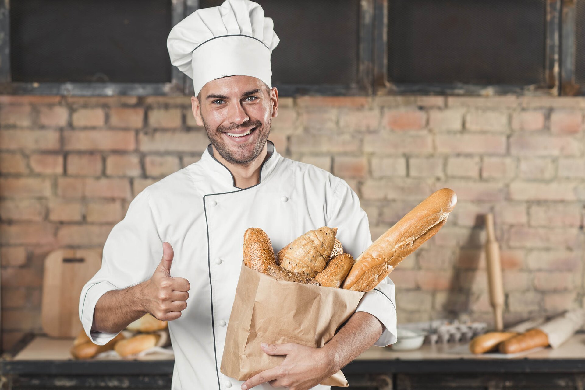 Na zdjęciu osoba ubrana w strój kucharza trzymająca pod pachą torbę z pieczywem. 