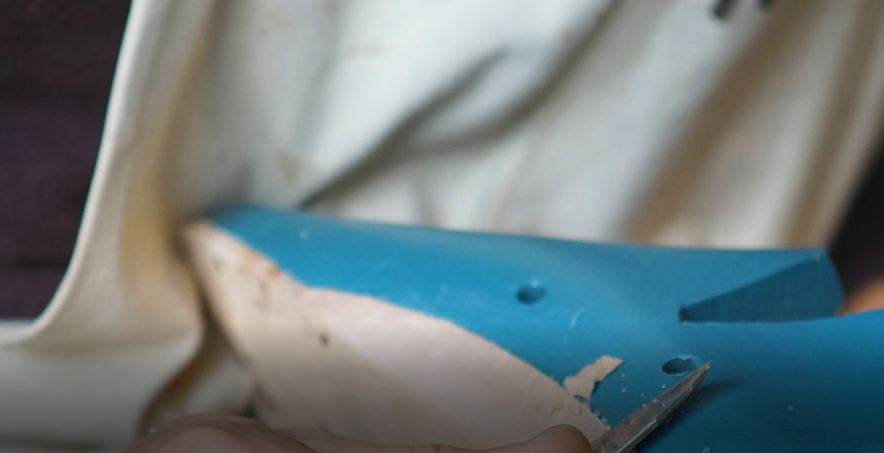 Zdjęcie przedstawia niebieski drewniany klocek, imitujący but, na który jest nałożony kawałek materiału, z którego przygotowuje się podpodeszwę. Nagranie tożsame z treścią.