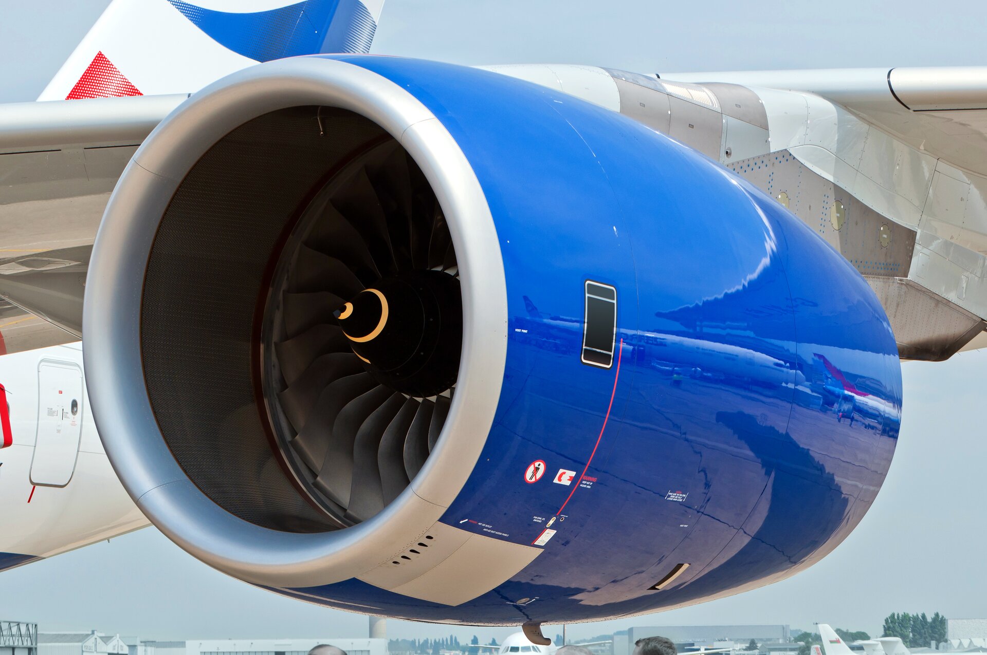 Zdjęcie przedstawia silnik odrzutowy na skrzydle samolotu pasażerskiego. Kadłub pomalowany jest na kolory biały i niebieski, natomiast wnętrze turbiny jest czarne z fantazyjną pomarańczową spiralą na samym czubku osi tak zwanego wentylatora, czyli przedniej obracającej się części.