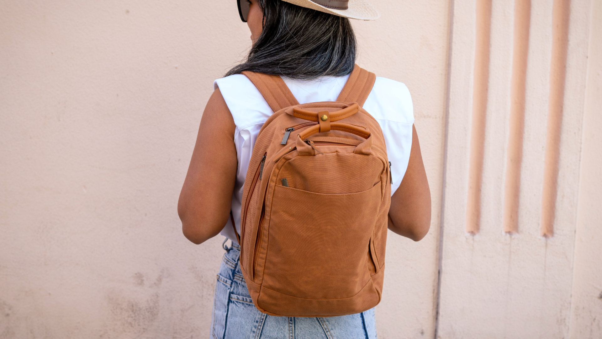 Na zdjęciu znajduje się dziewczyna, która stoi plecami do kadru. Dziewczyna ma na sobie plecak. Ubrana jest w jasną koszulkę bez rękawów i jasne jeansy. Na głowie widoczny jest kapelusz.