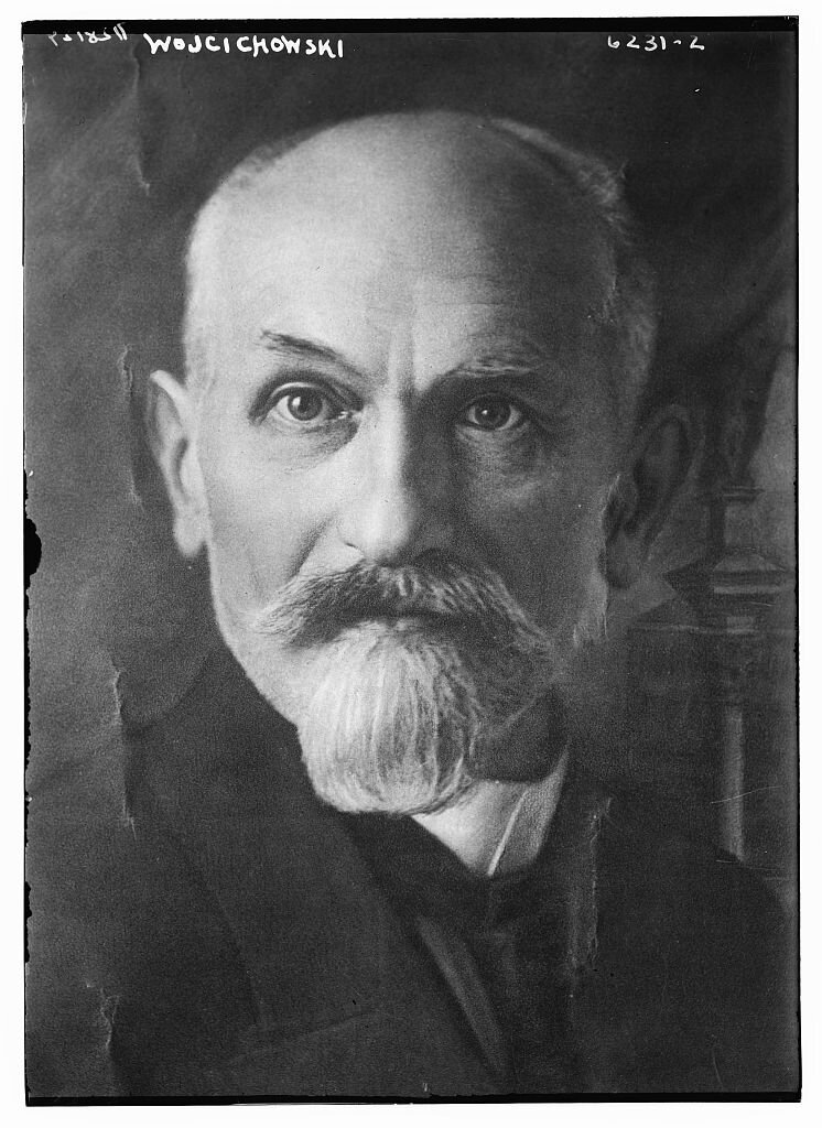 Zdjęcie przedstawia portret mężczyzny. Jest łysiejący, ma siwe włosy, brodę i wąsy. Ubrany w marynarkę, kamizelkę, koszulę ze stójką. Zdjęcie jest podpisane na górze: Wojciechowski.