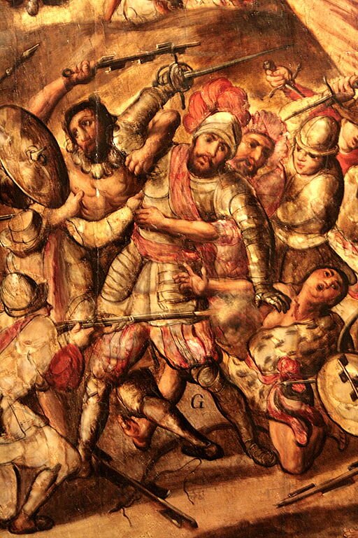 Ilustracja przedstawia scenę z bitwy. Po środku żołnierz w zbroi i metalowym hełmie z pióropuszem objęty przez kilku Indian. Żołnierz wymachuje szablą i próbuje się uwolnić. Z tyłu widać innych żołnierzy próbujących mu pomóc.