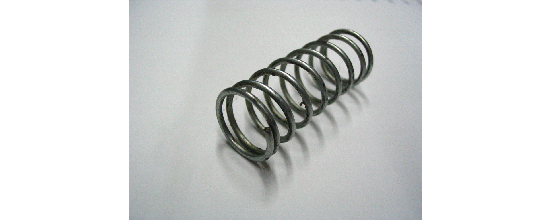 Zdjęcie sprężyny na białym tle. Sprężyna jest wykonana z grubego pręta.